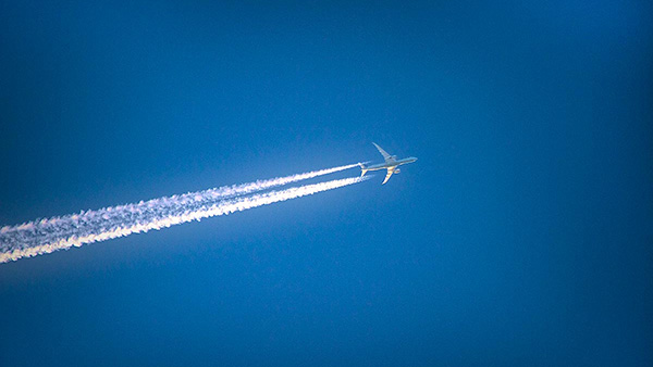 Am blauen Himmel fliegt ein Flugzeug, dass Kondensstreifen hinterlässt.